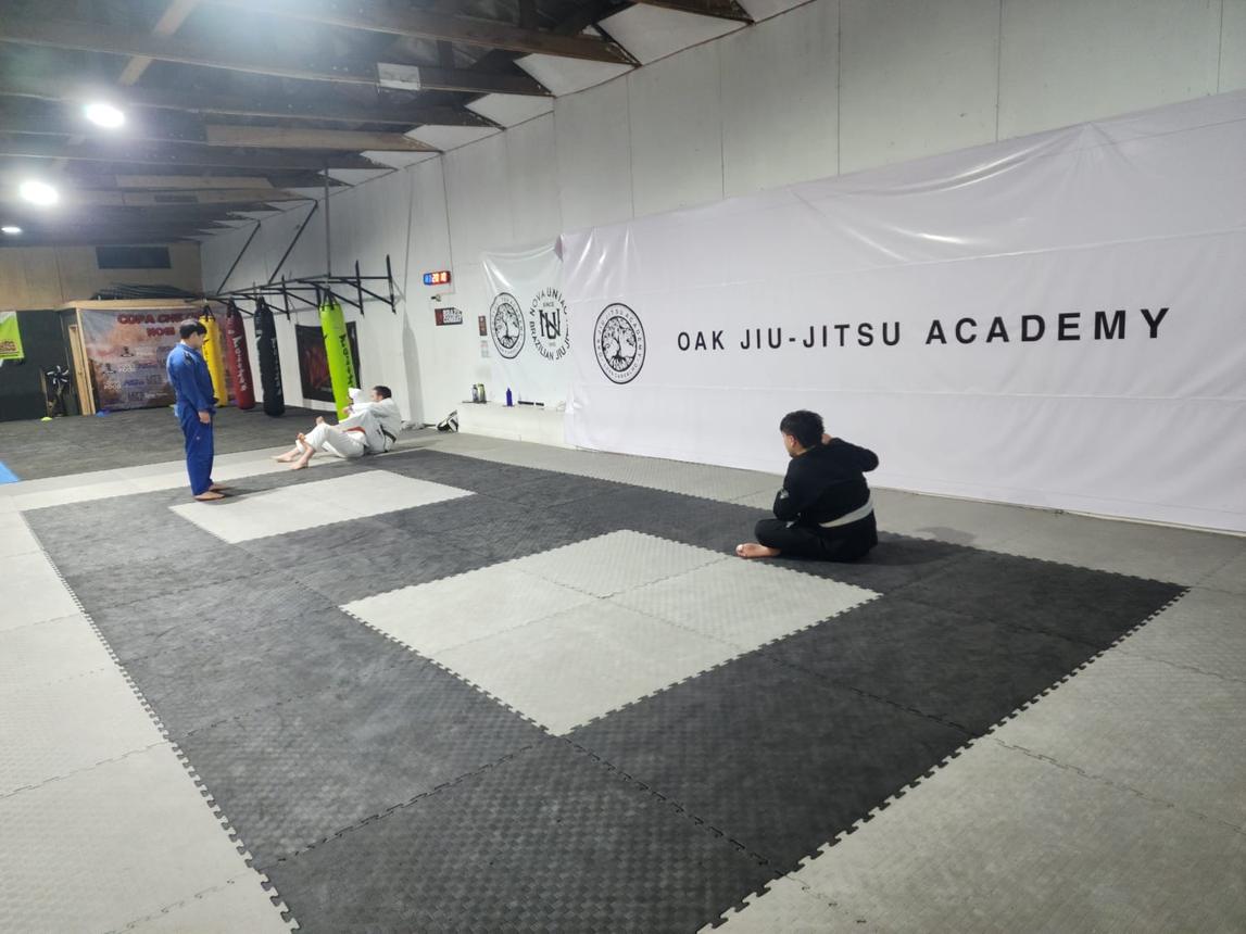 Tatami de Valhalla con los lienzos de Oak Jiu-Jitsu Academy y sacos de boxeo al fondo